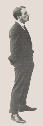 Profile of a young man standing with his hands in his pockets.