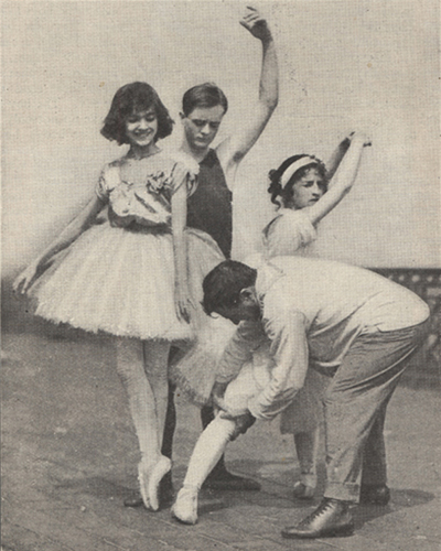 A male ballet instructor working with one of his pupils while several others look on.