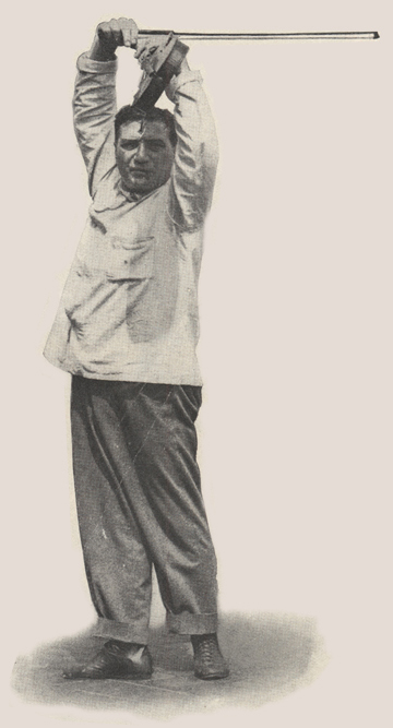 Male ballet instructor holding violin and bow over his head.
