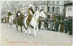 Three Native American men wearing traditional regalia riding on horses