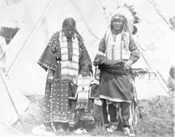 Native American man, woman, and child in traditional regalia in front of tipi