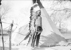 Native American man in front of tipi