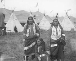 Three Native American men in beaded clothing in front of tipis