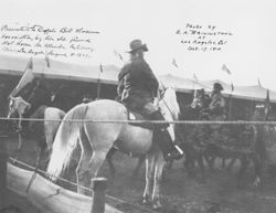 William F. Cody on gray horse with other riders in arena, Buffalo Bill's Wild West